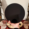 A hand holds a natural obsidian mirror, with other skulls and dark stones visible in the background.