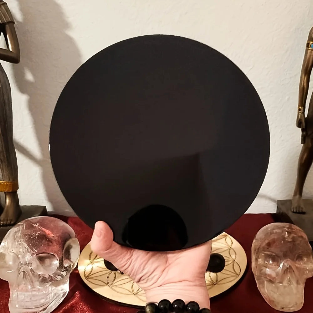 A hand holds a natural obsidian mirror, with other skulls and dark stones visible in the background.