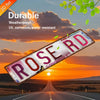 Vintage Retro Metallwandtafel in Form eines Wegeschilds mit der Aufschrift ROSE RD vor einer Sonnenuntergangslandschaft.
