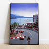 A panoramic photograph of a motorsport racing track with cars and spectators on a coastal road under a blue sky.
