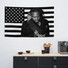 A man with dreadlocks is pictured against an American flag tapestry banner.