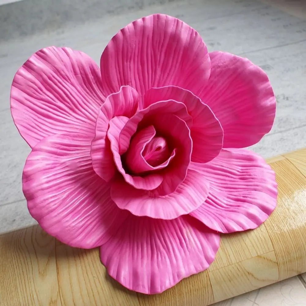 A vibrant pink silk foam rose flower with ruffled petals resting on a wooden surface.