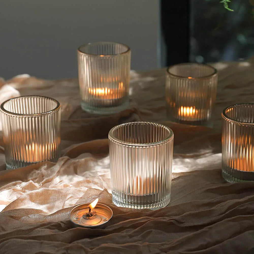 A collection of vintage striped glass votive candle holders resting on draped brown fabric.