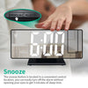A hand presses a Snooze-Light projection button on a digital alarm clock displaying 6:00 AM.
