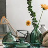 A set of three clear glass mini vases in various shades of green and yellow sitting on a dark book.