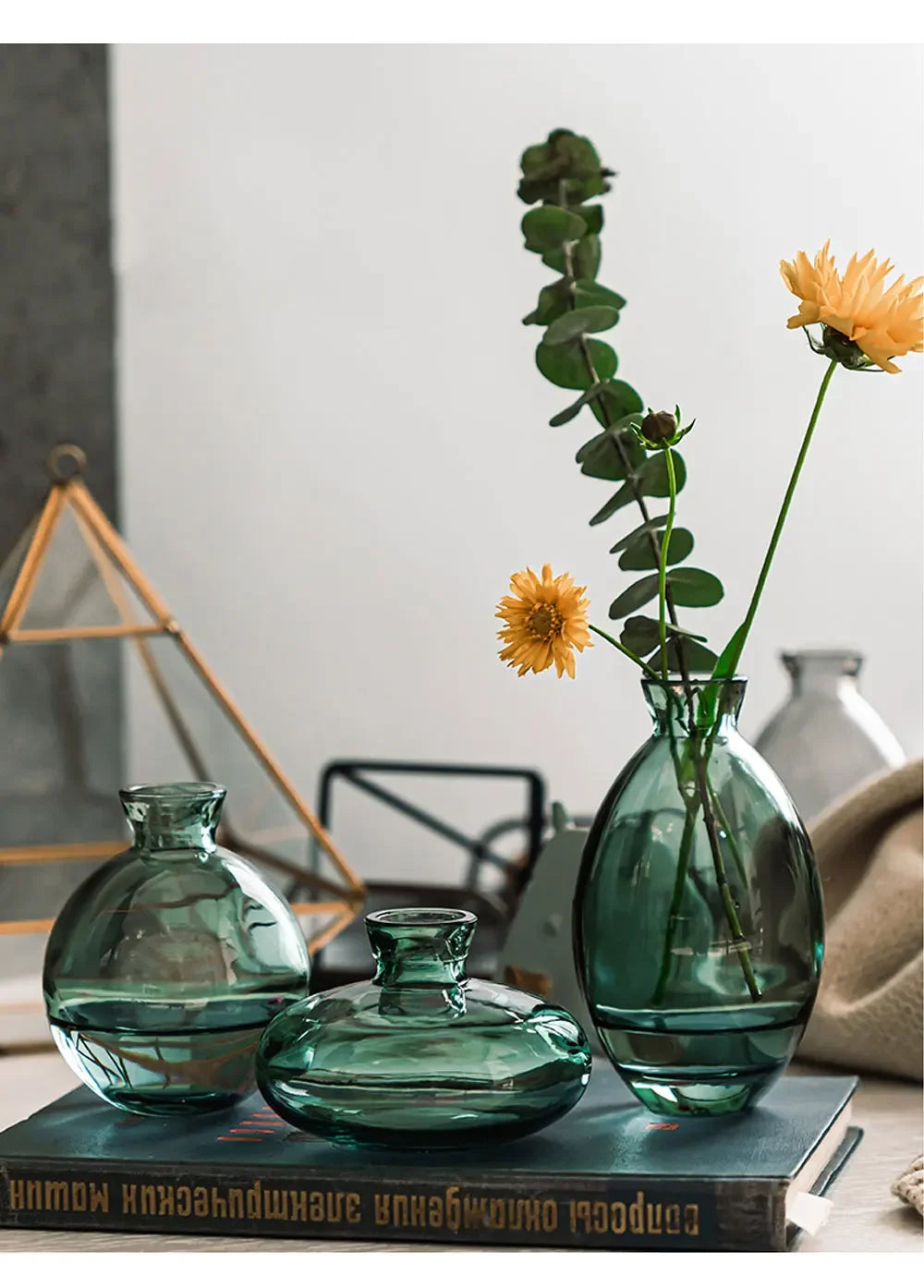 A set of three clear glass mini vases in various shades of green and yellow sitting on a dark book.