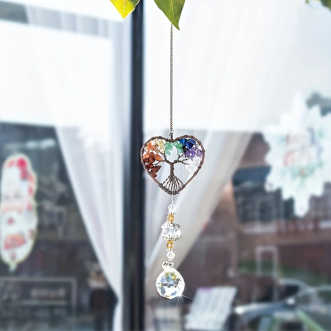 A hanging crystal tree of life sun catcher with colorful crystals suspended by a delicate chain.