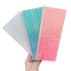 A hand holds three colorful striped paper drinking straws: teal, pink, and iridescent white.