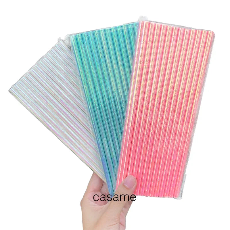 A hand holds three colorful striped paper drinking straws: teal, pink, and iridescent white.