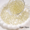 A clear glass measuring spoon holds small round yellow beads scattered on a white dish.