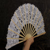 A white lace folding hand fan with a black background and light yellow ribs is being held.