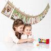A girl and a baby are interacting with a banner featuring monthly photos for a first birthday growth record.