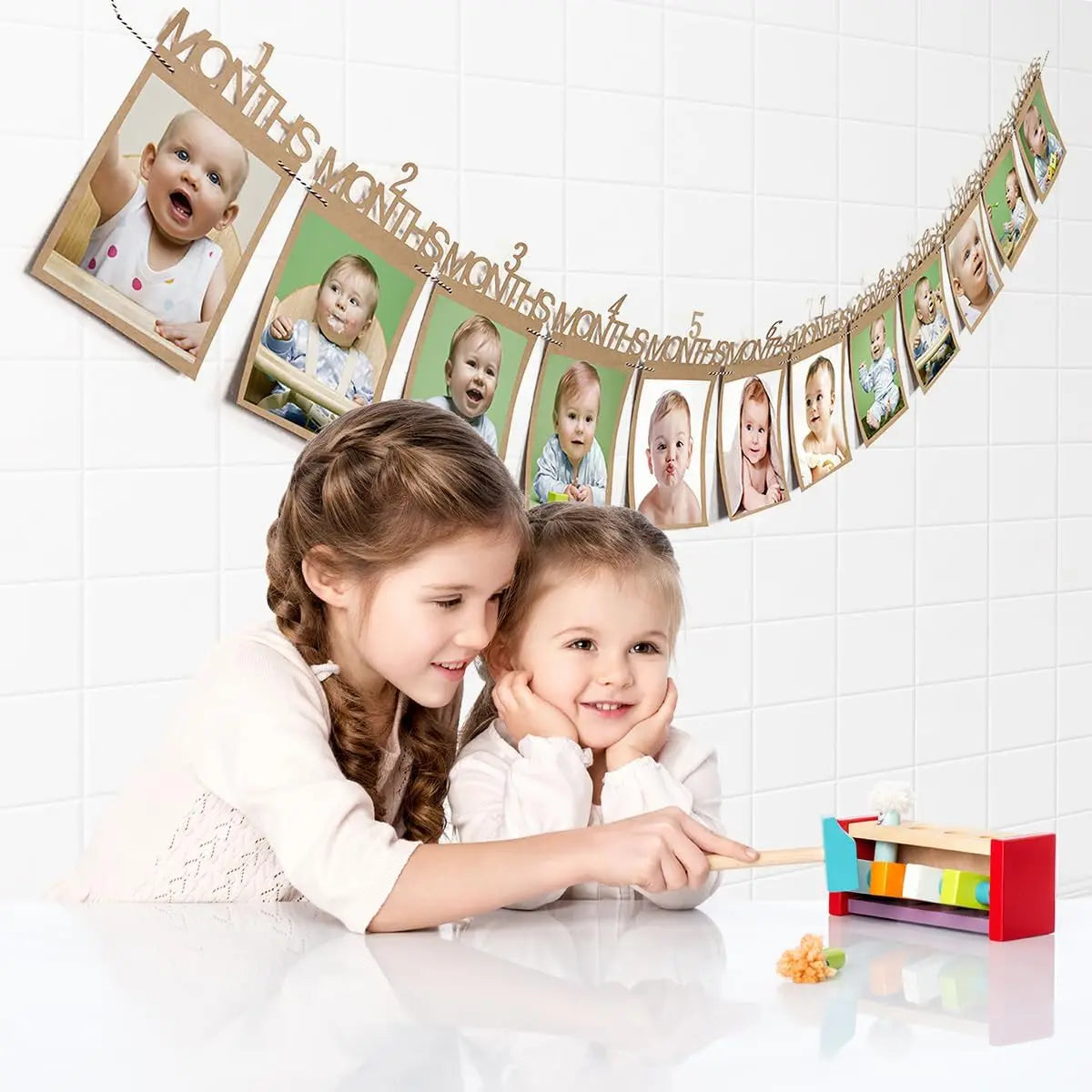 A girl and a baby are interacting with a banner featuring monthly photos for a first birthday growth record.
