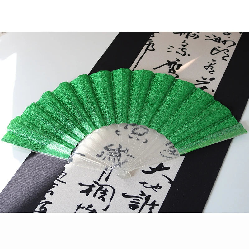 A green glitter folding fan with transparent ribs is displayed against a black background with Japanese calligraphy.