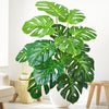 A vibrant artificial monstera plant with large green silk leaves displayed in a white pot on a wooden surface.