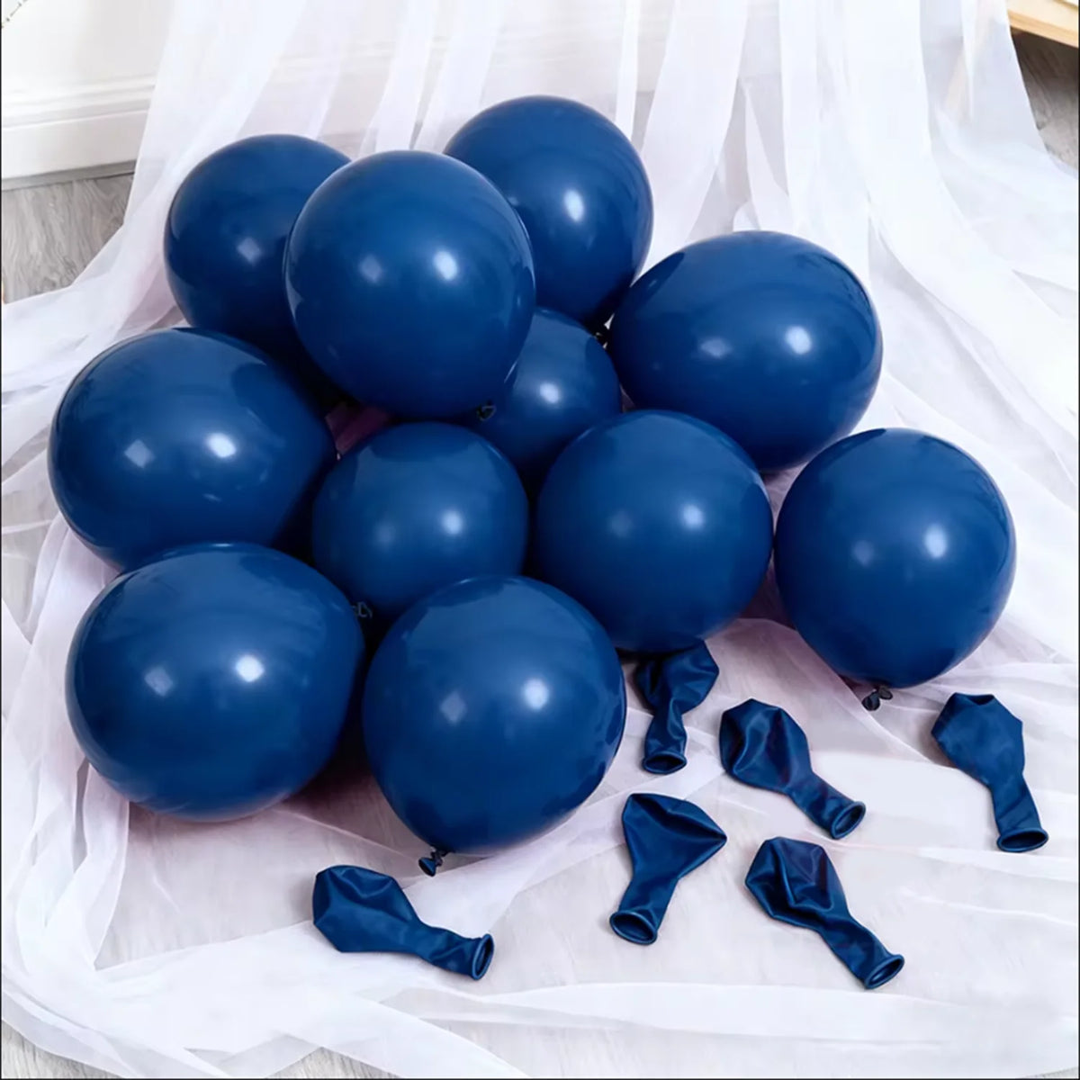 A cluster of dark blue latex balloons and blue ribbon streamers laid on white fabric.