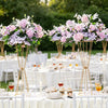 Gold geometric flower stands with pink and purple flowers decorating a white table setting.