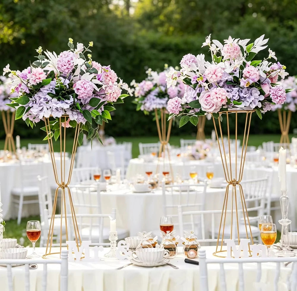 Gold geometric flower stands with pink and purple flowers decorating a white table setting.