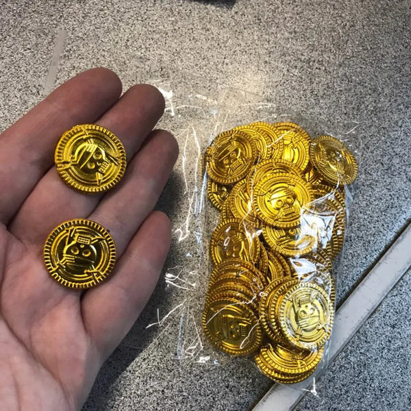 A hand holds a clear plastic bag filled with numerous gold pirate themed coins.