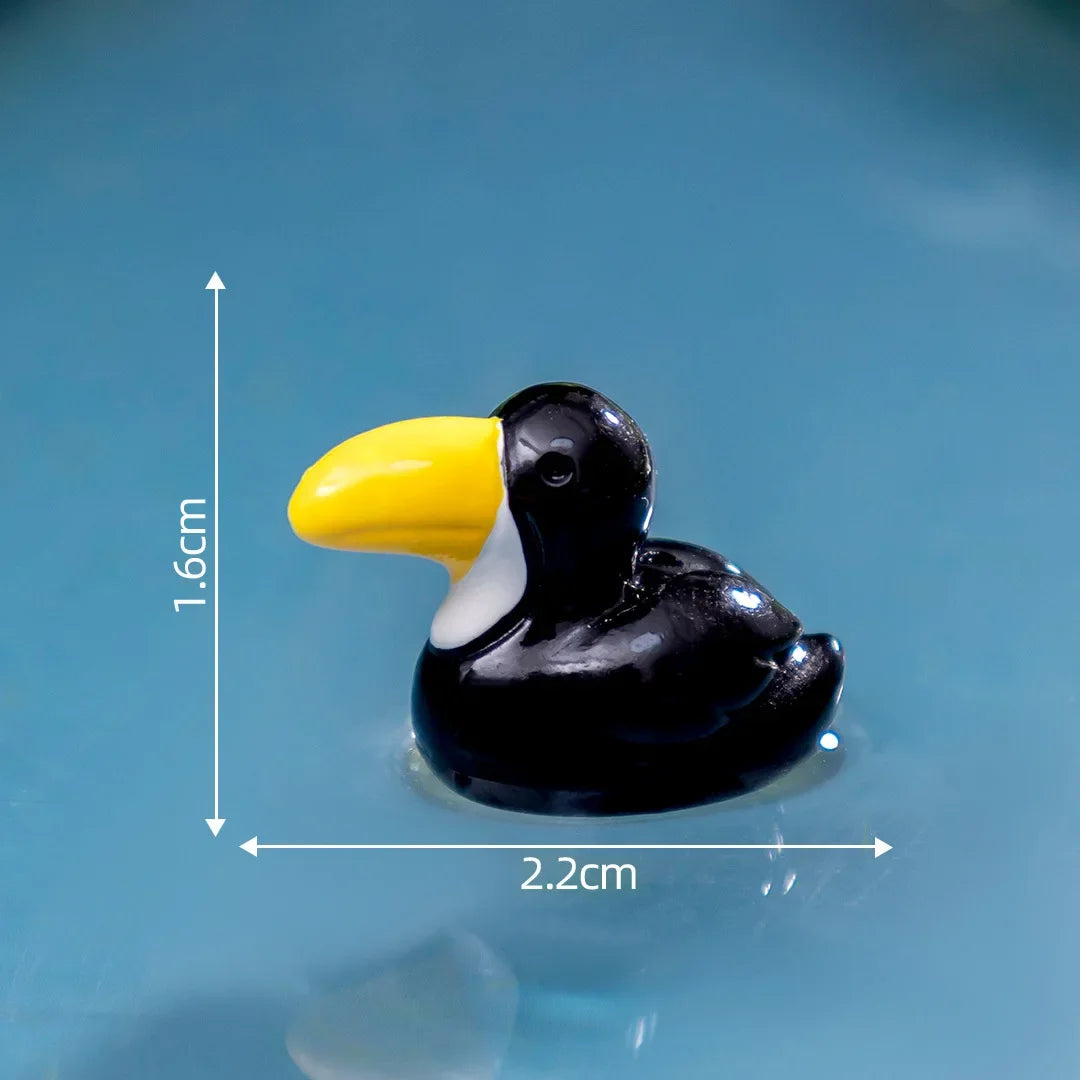 Petite sculpture d'animal en résine noir et jaune, possiblement un oiseau ou un canard, sur fond bleu.