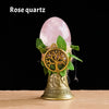 A rose quartz crystal is placed inside a golden chime shaped like a tree of life for meditation and decor.