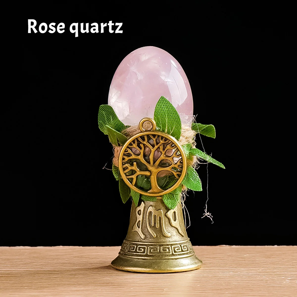 A rose quartz crystal is placed inside a golden chime shaped like a tree of life for meditation and decor.