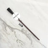 A dark metal magic wand replica with a textured handle and a metal core resting on a white marble surface.