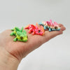 A hand holds several brightly colored articulated baby dragon figurines in shades of green, pink, and blue.