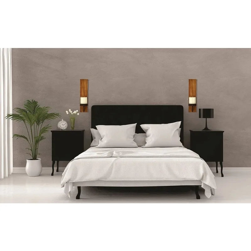 A bedroom setting featuring a black headboard, white bedding, and two wooden wall candle holders on a gray wall.