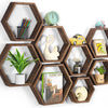 A set of four wooden hexagon floating shelves displaying various decorative items like pencils, a sculpture, and a small toy 