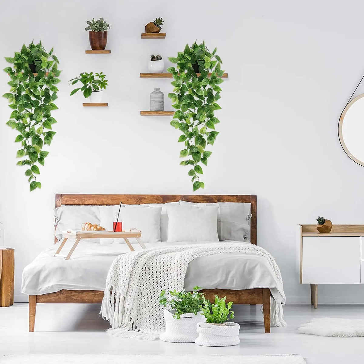 Artificial pothos hanging vines in a white pot displayed on a wooden bed frame with greenery wall decor.