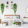 Artificial pothos hanging vines in a white pot displayed on a wooden bed frame with greenery wall decor.