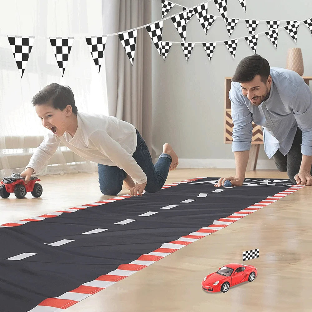 A man and a boy play with a red race car on a black checkered mat indoors.