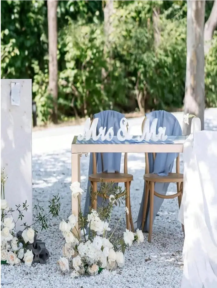 Wooden Mr & Mrs decorative letters for weddings displayed on a rustic table surrounded by white flowers.