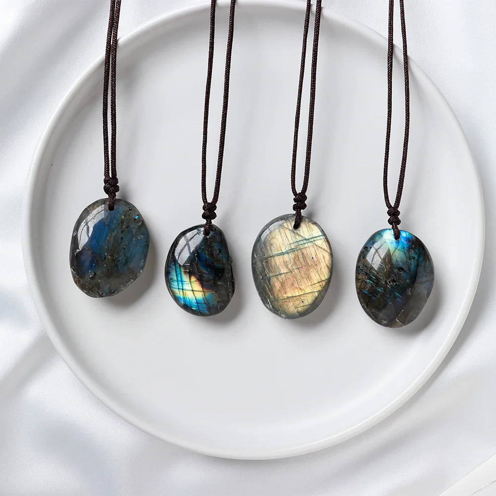 Four labradorite pendant necklaces with dark blue and gold iridescence displayed on a white plate.