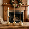 A set of three gold waterdrop design candle holders displayed on a wooden surface in front of a fireplace mantel.