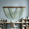A bohemian macrame wall tapestry featuring light mint green cord hanging above a wooden desk.