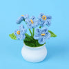 A bouquet of hand-woven blue crochet flowers in a white pot against a light blue background.