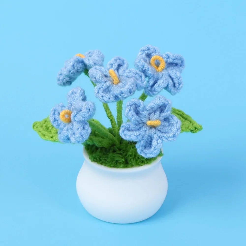 A bouquet of hand-woven blue crochet flowers in a white pot against a light blue background.