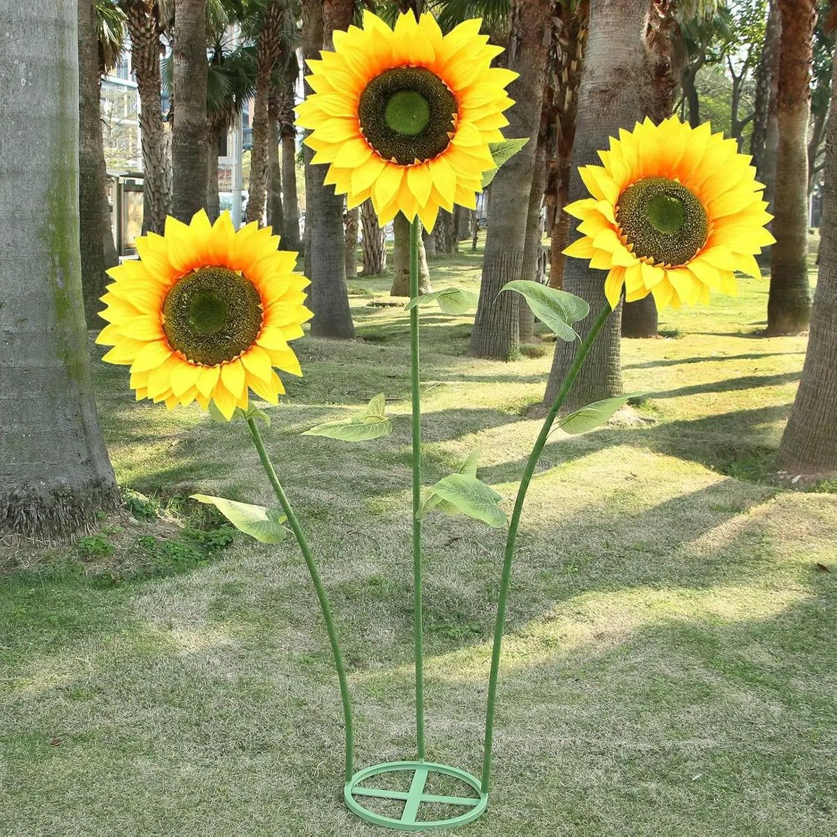 A bright yellow sunflower with a dark center stands on a metal base in a grassy outdoor setting.
