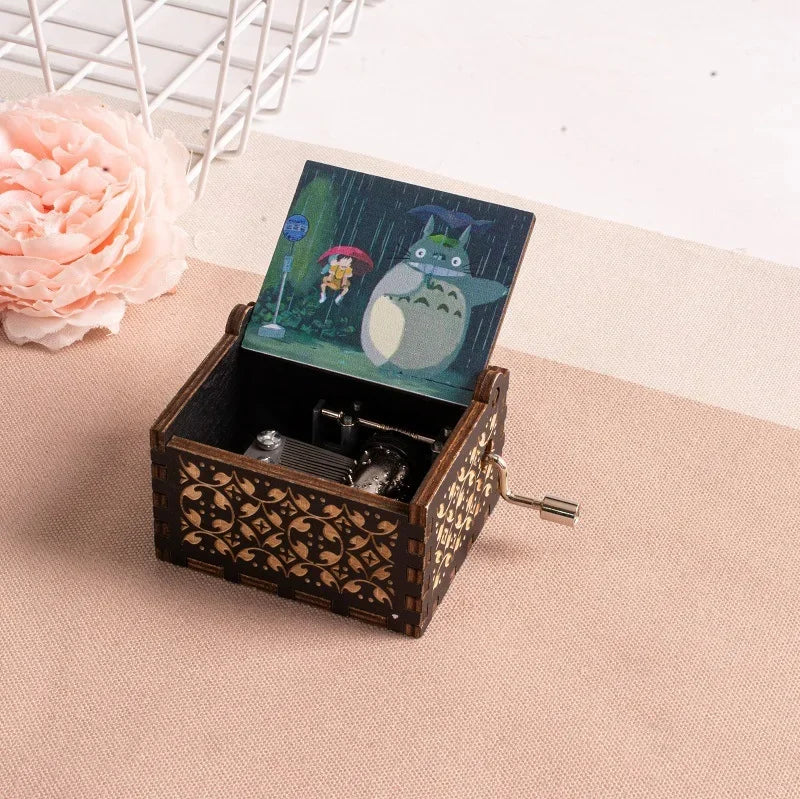 A hand-cranked wooden music box featuring a Totoro design, set against a pink floral background.