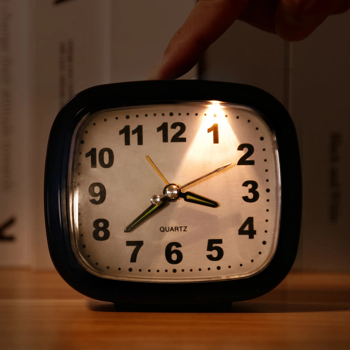 A close-up of a black analog alarm clock with a luminous display showing the time, being touched by a finger.
