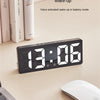 A black LED digital alarm clock displaying 13:06 is shown on a light surface next to a laptop and a white mouse.