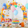 A colorful balloon arch decoration featuring yellow, orange, blue, and white balloons on a table.