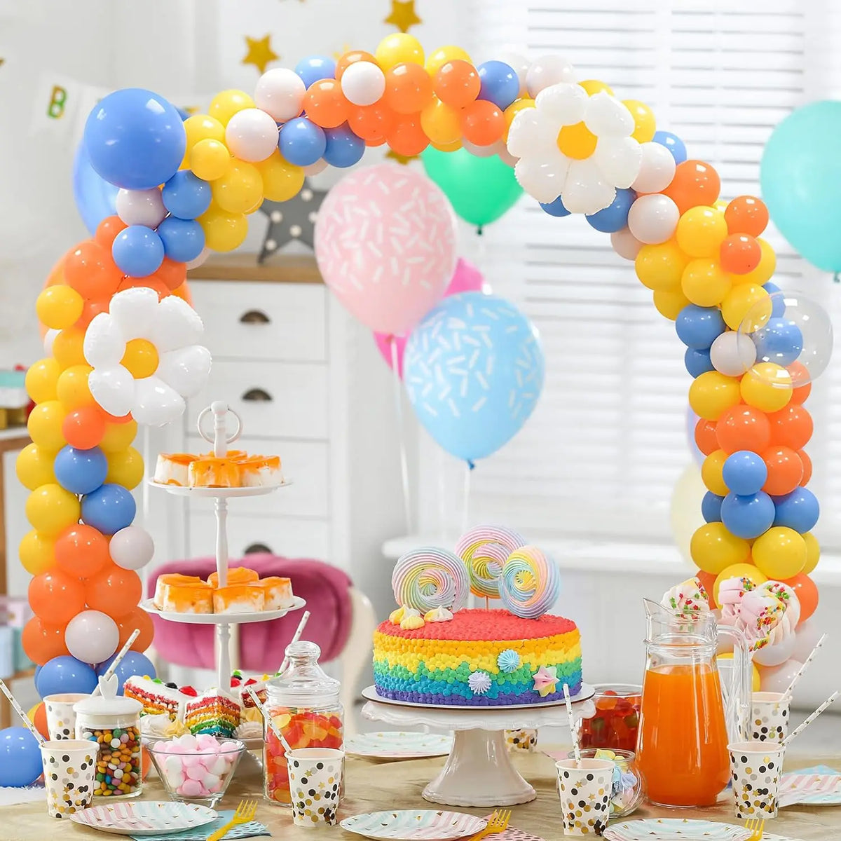 A colorful balloon arch decoration featuring yellow, orange, blue, and white balloons on a table.