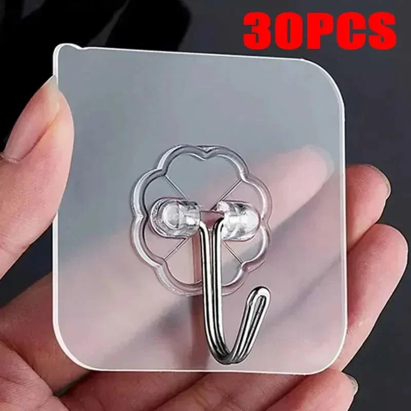 A hand holds a clear adhesive sheet with multiple silver-colored wall hooks and loops on it.