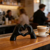 A black heart hand sculpture is placed on a wooden counter in a cafe setting.