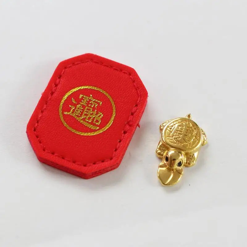 A red felt tag with gold lettering and a small golden tortoise figurine.