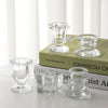 A collection of clear glass candle holders and candlesticks displayed on a stack of books.
