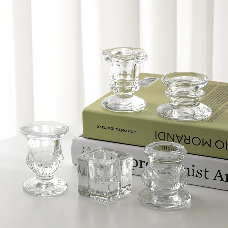 A collection of clear glass candle holders and candlesticks displayed on a stack of books.
